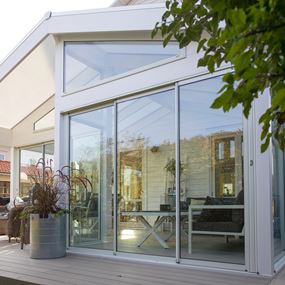 Veggtilsluttet, stilren hagestue i hvit med hvite skyvedørspartier i glass.