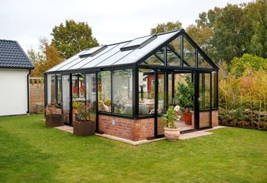 Et sort drivhus på veggen med dør på langsiden og gavl.